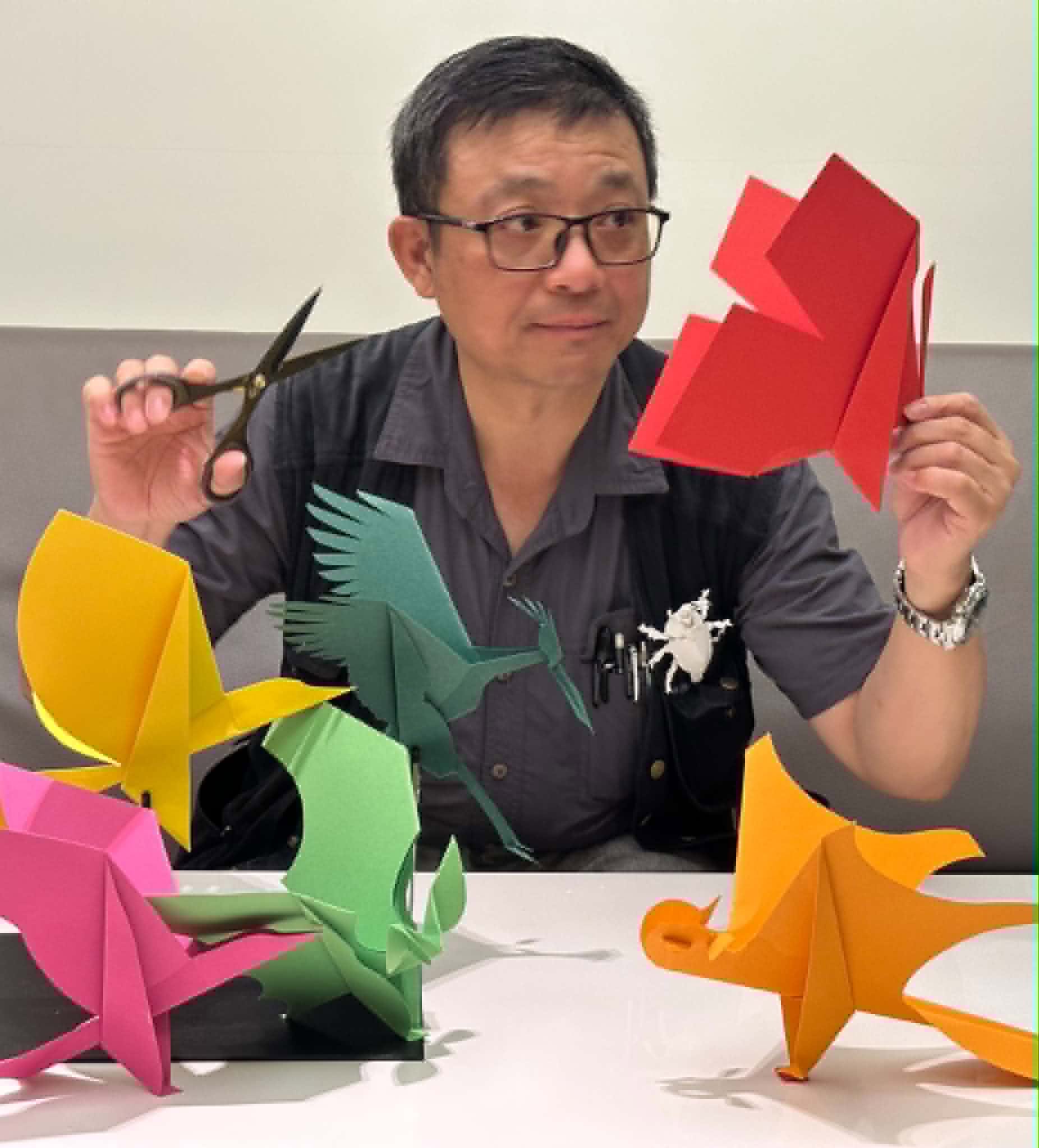 洪新富老師手持剪刀與彩色紙雕動物創作